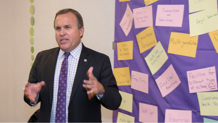 Casey Gwinn of Alliance for HOPE speaking in front of a wall covered with colorful sticky notes featuring topics like victim support facilities.